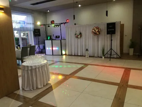 Stanowisko DJ-a obok ścianki z kwiatami, na pierwszym planie stolik z kieliszkami
